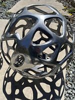 Close-up of a metal hollow spherical sculpture with geometric open lattice design casting shadows on the ground.
