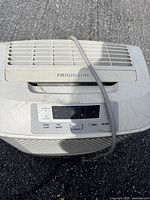 Top view showing control panel and Frigidaire logo on the large white dehumidifier with visible wear and electrical cord.