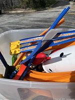 Top-down view of a clear plastic bin filled with orange Hot Wheels track pieces and some red and white plastic parts.