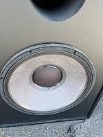 Close-up photo of the subwoofer speaker cone showing the visible JBL driver with some wear on the cone edge.