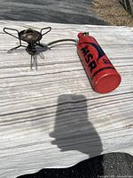 MSR WhisperLite camp stove connected to red fuel bottle on white surface with outdoor background