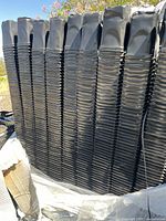 Tall stacks of black plastic quart size nursery pots on a pallet, showing the height and quantity of pots included in the lot.