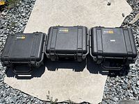 Three black Pelican cases closed, displayed outside on stone surface.