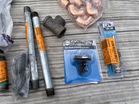 Photo showing three black iron pipes, tub drain stopper, a galvanized coupling, and some small fittings packaged in plastic