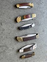Top view showing six folding pocket cutters arranged side by side on a concrete surface.