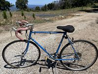 Full side view of the blue Schwinn road bike on a gravel road with natural landscape background.