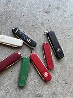 9 small Swiss Army knives in multiple colors arranged on a surface, with visible wear on some.