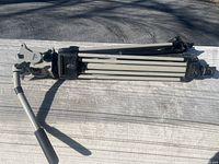 Folded Vinten tripod showing extendable legs, pan handle, and fluid head assembly on wooden surface.