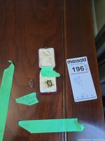 Two gold pins placed on wooden surface, one in maroon case with green label '10K' and another smaller pin labeled 'Royal Crown Plums' with green label 'gold filled pin'.