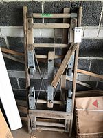 Folded antique rolling frame made of wood with attached metal parts, showing wear and a broken wooden piece.