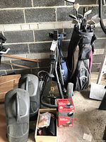 Overall view showing Callaway golf bag filled with various golf clubs and folded PGA golf cart with two plastic covers and other items on floor.