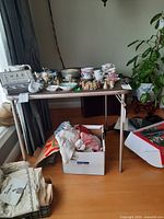 Foldable metal card table with various items displayed on and around it, including a box of clothes and assorted small decorative items, which are not part of the lot.