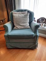 Front view of green velveteen armchair with two cushions, showing armrests, skirted bottom and floor setting.