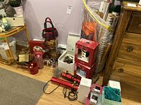 Photo showing various Christmas decorations including woven baskets, wrapped gifts, red candles, light strings, Santa figure, and gift wrap rolls on floor and shelves.