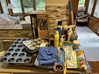 Lot items including mop, cleaning sprays, cloths, baking trays, and knife set on kitchen counter.