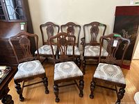 Full view of set of 6 dining chairs including 5 armless and 1 armchair standing on hardwood floor near wall.