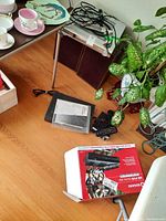 View of Satellite receiver, remote controls, battery chargers and cables on floor and small stand.