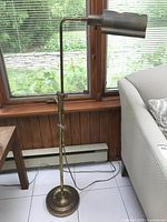 Full view of vintage metal floor lamp showing round base, adjustable pole, arm and lampshade with visible tarnish.