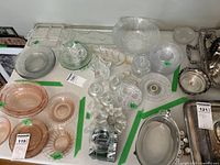 Overview of assorted pressed and cut glass items including plates, candle holders, serving ware and jam jar in clear and pink glass, arranged on a surface.