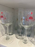 Stemmed wine glasses with red and white commemorative 1902-1992 print, 2 tall pilsner glasses behind them with gold lettering, several clear short drinking glasses.
