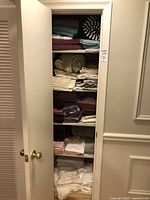 View of linen closet with shelves containing folded towels, sheets, pillowcases, and linens in multiple colors such as burgundy, teal, cream, and white.