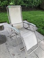 Outdoor lounge chair on a stone patio with green grass background, showing the full chair and its condition.
