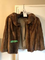 Front view of a brown mink fur jacket hanging on a hanger with the tag visible, showing the jacket is size small and has wear.