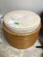 Full view of round rattan ottoman with beige fabric top cushion, tagged for sale.