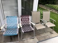 Four outdoor folding chairs on patio, two with woven straps and two with mesh seats and backs, showing wear and some rust.