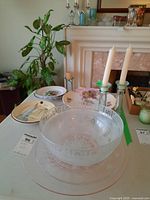 Wide shot of glass bowl, porcelain plates, floral platter, and two glass candle holders with white taper candles on table.