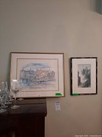 Wide view showing both framed prints side by side on display with wine glasses in foreground.