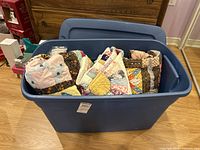 Large blue plastic storage bin filled with quilts and comforter/sleeping bag, shown from front