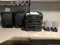 Full view of RCA stereo system stacked with two large RCA speakers to the left and two small silver Harman/Kardon speakers to the right on a countertop.