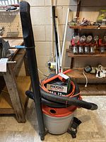 Full view of Ridgid shop vacuum with hose and attachments attached, placed on a floor with surrounding workshop items.
