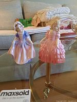 Photo showing both Royal Doulton figurines on a glass table, background includes couch and folded linens.