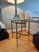 Side table with glass top and metal base with decorative feet and casters