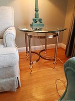 Side view of the metal base and glass top side table next to a couch, showing the curved metal supports and caster wheels.