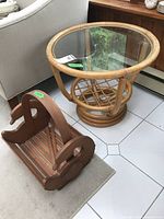 Photo of circular bamboo style side table with glass top alongside wooden goose motif magazine holder on tiled floor.