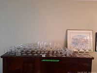 Wide shot of a piano top filled with various crystal glasses including wine glasses, martini glasses, vases and shot glasses arranged in rows.