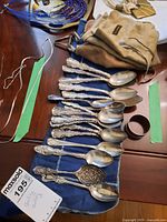Overall view of spoons laid out on blue cloth with a small cylindrical napkin ring visible at right.