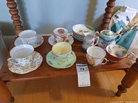 Wide view showing entire set of teacups, saucers, plates, creamer, and bowl on wooden table, displaying variety of floral patterns and colors