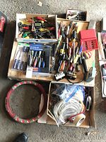 Wide view of the tool lot showing scattered screwdrivers, drill bit sets, and cable connectors in boxes