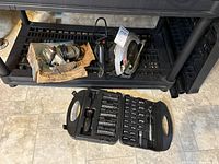 Photo capturing all three items: Skilsaw circular saw, vintage jigsaw in original box, and screwdriver/ratchet set with bits laid out on floor under shelving unit.