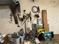 Workbench and pegboard with various tools including hand saws, hand drill, clamps, yellow extension cords, and a green electric bench grinder.