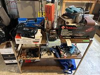 Wide view of all included tools displayed on a metal shelving unit showing brand names and accessories (power cords, sanding belts).