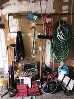 Wide shot of hanging garden hoses, assorted garden tools, tool cases, and Jobmate air compressor on floor