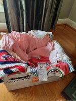 Box containing folded vintage baby clothes including pink and white rompers, a smocked dress, and other vintage fabric garments.