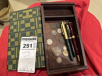Wooden box with vintage foreign coins and three pens inside