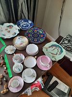 Overview of vintage espresso cups, saucers, and plates on a table with various floral and colorful designs showing condition and style