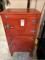 Front view of red painted wooden vintage ice box cabinet with two doors and metal latches, showing some wear and aging.